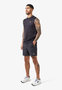 Schwarzes ärmelloses Sportshirt und Shorts. Das Outfit hat eine schlanke Passform, mit einem strukturierten Design und reflektierenden Akzenten auf dem Shirt.