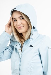 Jachetă waterproof de un albastru deschis, cu fermoar, glugă ajustabilă și logo-ul umbrelei negre pe piept. Textură netedă și design ajustat.