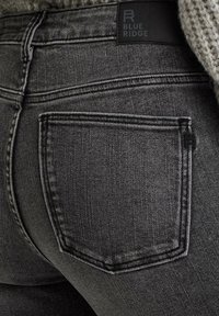 Graue Denim-Jeans mit subtiler Textur, ausgestattet mit einer einzigen Gesäßtasche und einem schwarzen Etikett mit "BLUE RIDGE" am Bund.