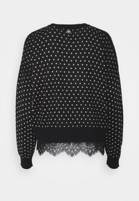 Musta neule, jossa on valkoinen tähtikuvio, pyöreä kaula-aukko, resorit hihansuissa ja pitsiyksityiskohta helmassa.