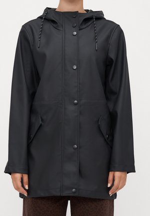 Imperméable noir à capuche à manches longues avec boutons-pression à l'avant et poches à rabat porté par une personne sur un fond uni.