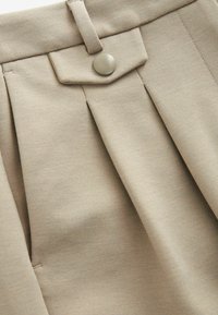 Beige suoraan lahkeisiin housuihin, joissa on sileä pinta, nappikiinnitys ja litteä vyötärö. Valmistettu pehmeästä, joustavasta kankaasta.