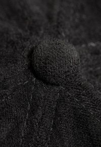 Tela negra texturizada con un botón circular prominente, con líneas de costura visibles y un aspecto general suave y peludo.