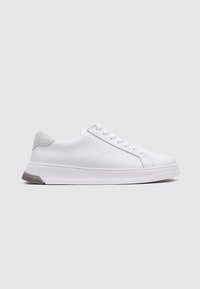 Zapatilla blanca de cuero con un acabado suave, acento de ante gris en el talón, punta redonda y suela plana de goma. Cuenta con siete ojales para los cordones.