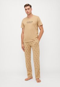 Beige pamut póló, fekete "POLO" felirattal; illeszkedő, könnyű mintás pizsamanadrág, amelyen kis, sötét logók találhatók bézs háttéren.