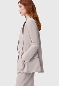 Gaiši bēša, pielāgota žakete ar brīvu piegriezumu, vienas pogas aizdare, ar iegriezumu atlokiem un sānu kabatām. Gluda tekstūra.