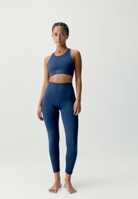 Námornícka športová podprsenka a legíny vyrobené z hladkej, elastickej tkaniny. Legíny majú textúrované akcenty pri členkoch.