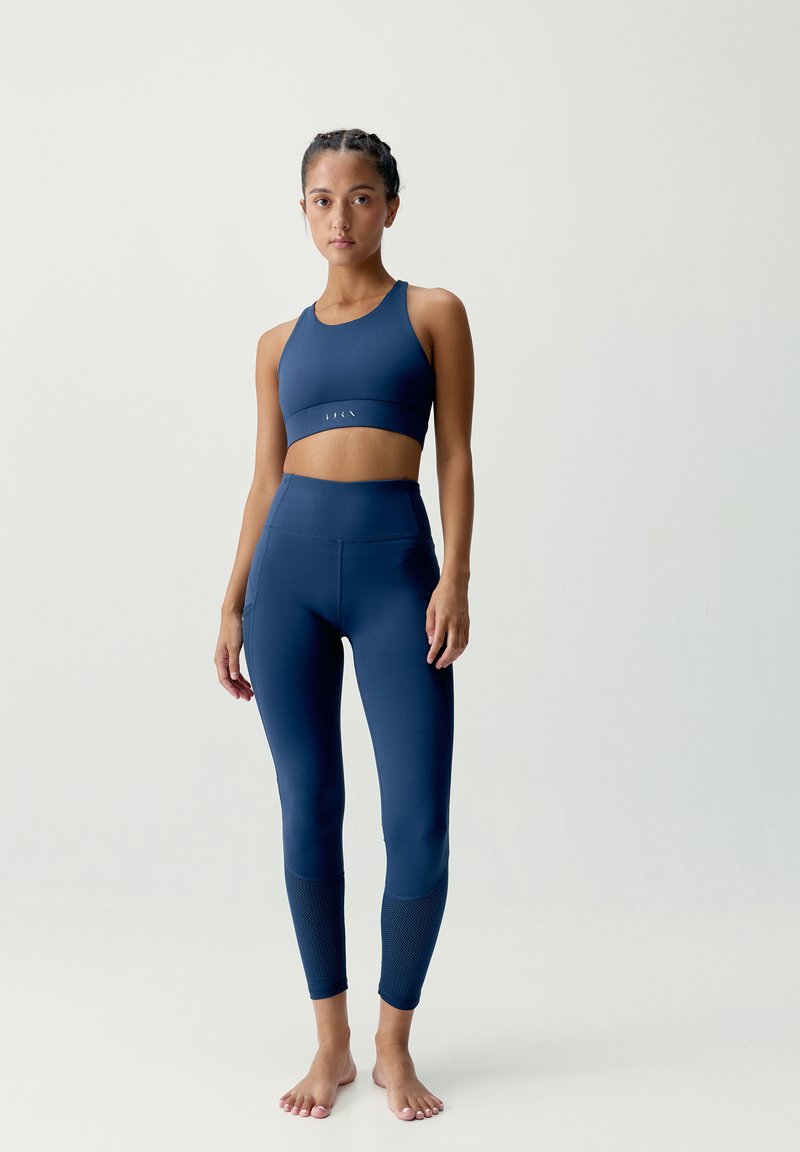 Námornícka športová podprsenka a legíny vyrobené z hladkej, elastickej tkaniny. Legíny majú textúrované akcenty pri členkoch.