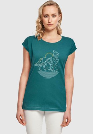 Türkisa T-Shirt mit umgeschlagenen kurzen Ärmeln, das ein weißes Grafikwild eines Greifs vor einem kreisförmigen, bergigen Hintergrund zeigt.