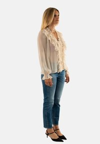 Blusa ligera y arrugada en tejido crema translúcido con mangas largas, combinada con unos vaqueros skinny azul medio y tacones negros con tiras.