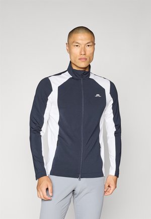 Navy and white zip-up jacket with a high collar, featuring side pockets and contrasting panel design. Made from a stretchy, smooth material.