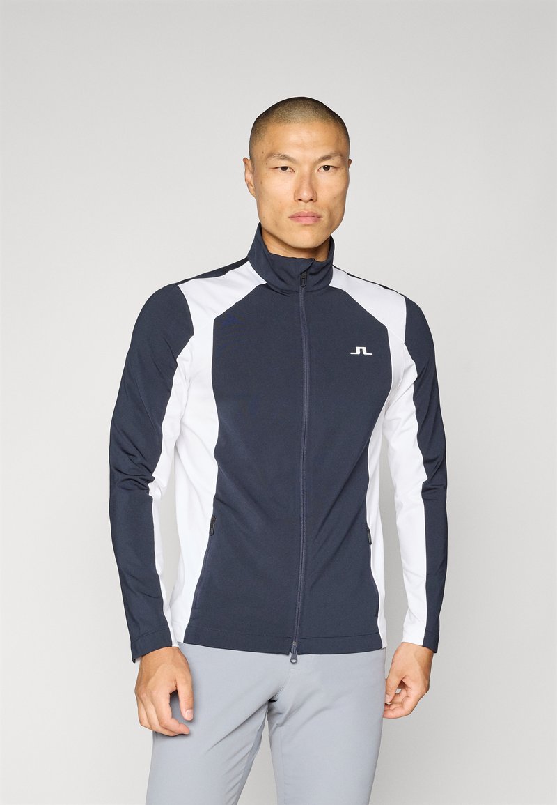 Navy and white zip-up jacket with a high collar, featuring side pockets and contrasting panel design. Made from a stretchy, smooth material.