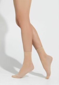 Calze alla caviglia trasparenti color carne con una texture liscia, dotate di una sottile fascia con logo sulla parte superiore. Progettate per un aspetto aderente e confortevole.