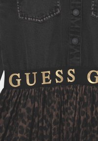 Czarna sukienka dżinsowa z guzikami na górze, z czarnym pasem w złotym napisie "GUESS" oraz plisowaną spódnicą z motywem lamparta.