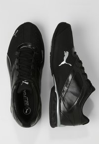 Des chaussures de sport noires avec un dessus en synthétique lisse, des accents perforés, une semelle intérieure rembourrée et des détails en logo argenté sur le côté.
