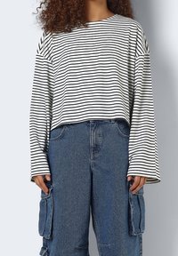 Gekürztes Langarmoberteil in Weiß mit schwarzen horizontalen Streifen; kombiniert mit hochtaillierten blauen Denim-Cargo-Hosen mit Seitentaschen.