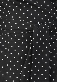 Tessuto nero con pois bianchi, con dettaglio della cintura annodata. Texture liscia e design aderente con cuciture visibili.