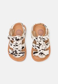 Dětské sandály s designem kravského vzoru v černobílé srsti, vybavené několika nastavovacími popruhy a koženou stélkou v barvě tan.