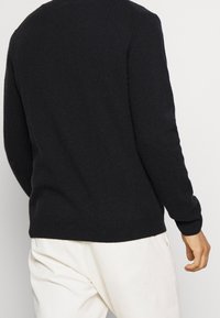 Svart stickad tröja med rund halsringning och ribbad nederkant. Tyget är mjukt med en lätt texturerad yta. Bärs tillsammans med ljusa byxor.