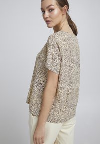 Top s leopardím vzorem v béžové a hnědé barvě, krátké rukávy, volný střih a měkký materiál. Stylizováno s světle zbarvenými kalhotami.