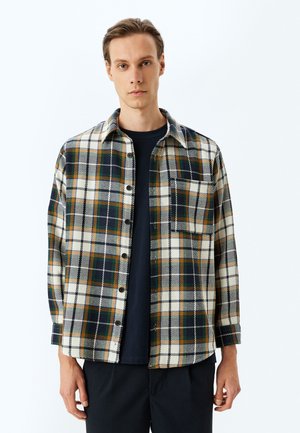 Button-up-paita, jossa on ruudullinen kuvio kermansävyssä, vihreässä, tummansinisessä ja oranssissa. Paita sisältää rintataskun ja pitkät hihat pyöristetyllä helmalla.
