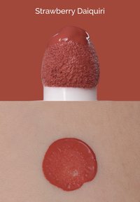 Applicatore per prodotto labbra con un applicatore morbido e vellutato, che stende un liquido spesso di colore rosso-rosa profondo sulla pelle, con una finitura liscia.