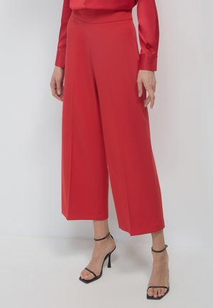 Red wide-leg trousers made of smooth fabric, featuring a high waist and a tailored fit, paired with black strappy heels.