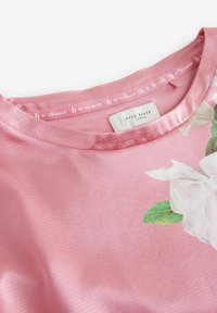 Short-sleeve pink shirt featuring a floral design, made from soft fabric. Round neckline with a smooth texture and brand label visible.