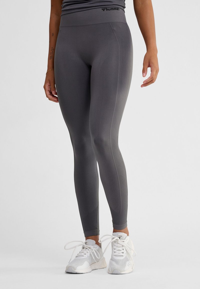 Grå atletiska leggings med hög midja, med ribbade detaljer längs sidorna och en slät struktur. Matcher med vita sneakers.