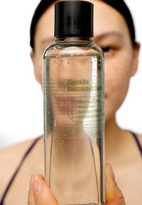 Klar glasflaske med et sort låg. Indeholder en gennemsigtig væske med bobler. Etikettekst i grønt identificerer den som "Centella Unscented Toner."