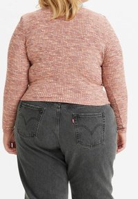 Pitkähihaista puseroa vaaleanpunaisesta teksturoidusta kankaasta, jossa on ruutumainen kuvio, on yhdistetty tummanharmaisiin farkkuihin, joissa on takataskut ja pieni logotarra.