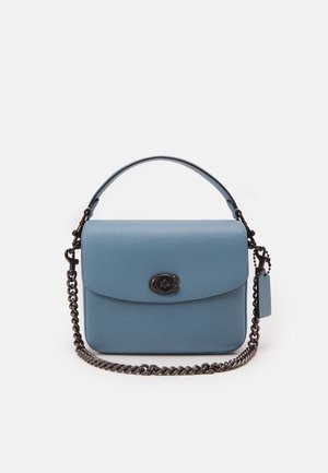 Blå læderhåndtaske med top håndtag, front drejelås og aftagelig sort metal kædestrop på hvid baggrund.