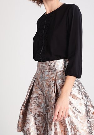 Woman wearing a black long-sleeve blouse paired with a high-waisted, metallic floral-patterned pleated skirt.