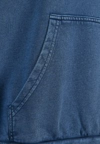 Tessuto blu scuro con una texture liscia presenta una tasca frontale e una cucitura prominente lungo i bordi, enfatizzando il suo design casual.