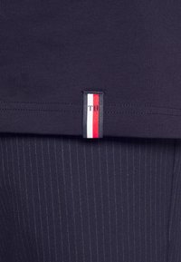 Námořnické bavlněné tričko s jemnou strukturou, se svislým pruhovaným štítkem v bílé, červené a modré barvě na lemu, spárované s pruhovanými kalhotami.