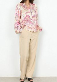 Blouse à manches longues en crème avec un motif paisley rose, col froncé et tissu doux, assortie à un pantalon large beige et des talons noirs.