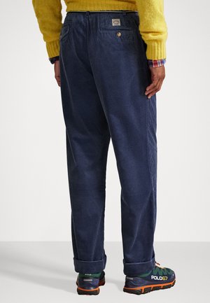 Marineblauwe corduroy broek met een relaxte pasvorm, voorzien van een achterzak met een logo patch en opgerolde mouwen, gecombineerd met meerkleurige sportieve schoenen.