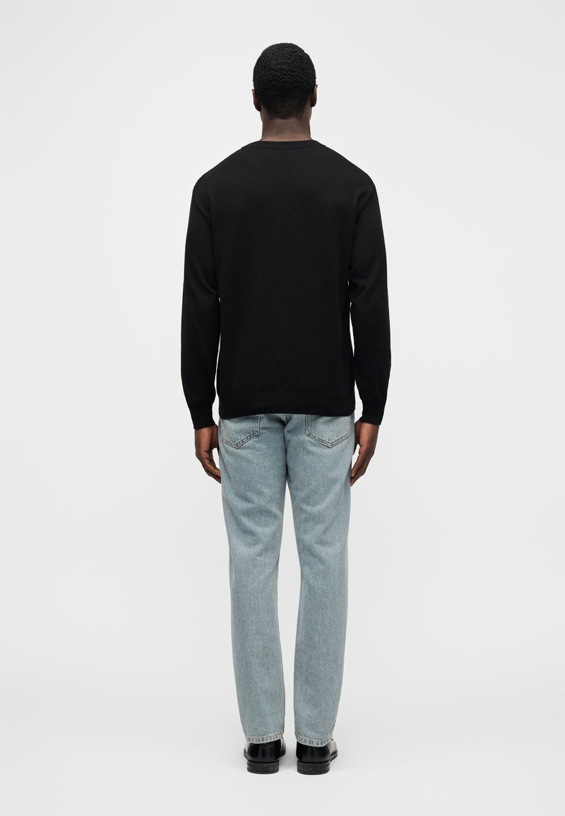 Schwarzer Pullover mit langen Ärmeln und rundem Ausschnitt. Kombiniert mit hellblauen Jeans mit geradem Bein und schwarzen Schuhen. Glatte Textur, minimalistisches Design.