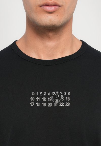 T-shirt en coton noir avec un graphisme blanc comportant des chiffres et un "6" entouré imprimé au centre. Encolure ras du cou, manches courtes.