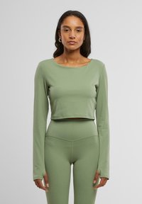 Zöld, cropped, hosszú ujjú felső sima, rugalmas anyagból; hozzá illő, magasító derekú leggings, varrási részletekkel.