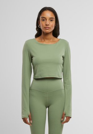 Grön, kortärmad topp med långa ärmar gjord av mjukt, stretchigt material; matchas med höga leggings med sömdetaljer.
