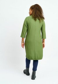 Olivgrön texturerad klänning med trekvartslånga ärmar, midilängd, med rak skärning, bärs över marinblå leggings och svarta anklarstövlar.