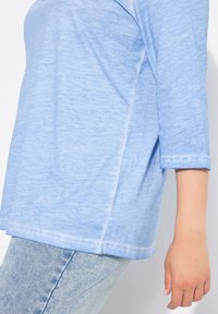 Světle modrý, volně střižený top s třičtvrtinovými rukávy vyrobený z měkké, texturované látky s postranním švem, kombinovaný se světle modrými džíny.