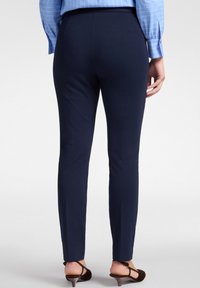 Pantalones tapered azul marino con una textura de tela suave, que cuentan con una cintura de altura media y un diseño a la altura del tobillo, combinados con sandalias marrones.