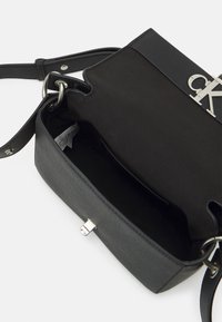 Borsa a tracolla nera in pelle con una texture liscia, hardware argentato e apertura superiore. Presenta un design leggermente strutturato e una tracolla regolabile.