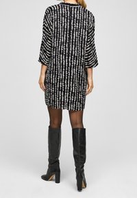 Svart och vit mönstrad klänning med trekvartslånga ärmar, med lös passform och rak nederkant, i kombination med svarta knähöga stövlar.