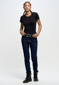 Musta lyhythihainen fitted-paita, joka on yhdistetty tummansinihin skinny-farkkuihin ja mustiin nauhakuviollisiin maihinnousukenkihin, ja sen kanssa on hopeinen solkivyö.