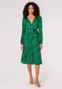 Robe portefeuille verte avec un motif tourbillonnant, des manches longues, une ceinture à la taille et une jupe fluide qui tombe sous le genou.
