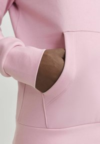 Pink sweatshirt featuring a large front pocket and ribbed cuffs, showcasing a soft fabric texture and a relaxed design with tailored seams.