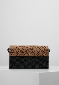 Sac à main tissé noir avec un rabat en cuir marron à motifs, doté de clous dorés et d'un design structuré. Forme compacte avec une bandoulière.